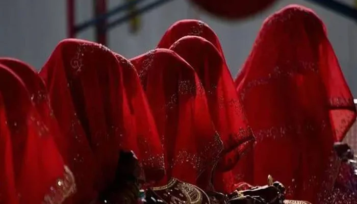 بھارت کی ریاست مدھیہ پردیش میں شادی کے نام پر مبینہ فراڈ کا انوکھا واقعہ سامنے آیا ہے، جہاں 40 سے زائد افراد دولہا بن کر اجتماعی شادی کی تقریب میں پہنچے، تاہم دلہنیں تقریب میں نہ پہنچیں۔ غیر ملکی خبر ایجنسی کے مطابق متاثرہ افراد کو ایک شخص نے خود کو شادی کے لیے رشتے کروانے والا شخص ظاہر کر کے دھوکا دیا۔ متاثرین میں شامل ابھشیک ورما کے والدین بھی اپنے بیٹے کے لیے دلہن تلاش کر رہے تھے، جب قریبی گاؤں کے ایک شخص نے ان سے رابطہ کر کے رشتہ کروانے کی پیشکش کی۔ مبینہ میچ میکر نے خاندانوں کو بتایا کہ انہیں صرف تصویروں کے البم میں سے ایک یتیم لڑکی کا انتخاب کرنا ہوگا اور اجتماعی شادی میں شرکت کے لیے تقریباً 200 ڈالر ادا کرنا ہوں گے۔ رپورٹ کے مطابق مئی کے آخر میں شادی کے روز تقریباً 40 دولہے، جن میں ابھشیک ورما بھی شامل تھا، صبح 8 بجے شادی کے لباس میں تقریب میں پہنچ گئے، تاہم کئی گھنٹے انتظار کے باوجود کوئی دلہن وہاں نہ پہنچی۔ شام تک دولہوں کو اندازہ ہوگیا کہ وہ مبینہ طور پر فراڈ کا شکار ہوچکے ہیں۔ پولیس افسر کے مطابق متاثرہ افراد کی عمریں 20 سے 40 سال کے درمیان ہیں اور ان میں زیادہ تر افراد دیہی علاقوں سے تعلق رکھتے ہیں۔ ان کا کہنا ہے کہ شرمندگی کے باعث کئی دیگر متاثرین نے ممکنہ طور پر پولیس سے رابطہ نہیں کیا۔ Bizarre wedding scam in India